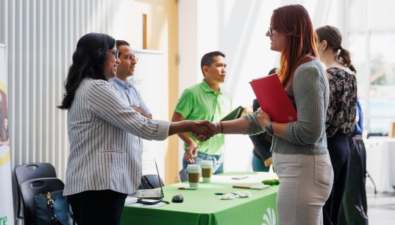 Student shakes hands with an employer at a job fair table.