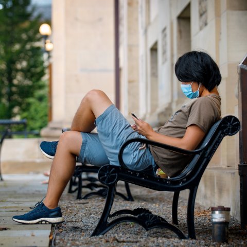 Student sitting on bench and wearing a mask